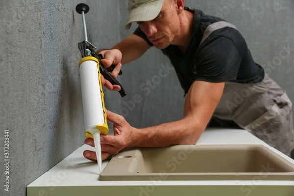 Obraz worker seals kitchen sink with sealant. hands of worker works with construction sealant gun in the kitchen. 