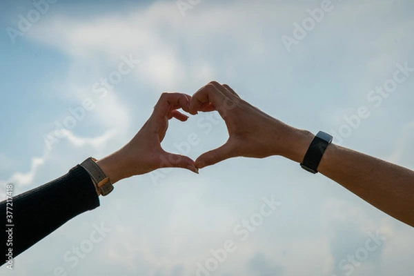 Obraz close up male and female hands making a heart shape silhouette in the sky.