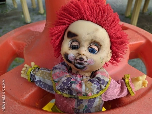 Fototapeta scary toy clown with red hair and half open blue eyes and outstretched hands in a plastic wheel