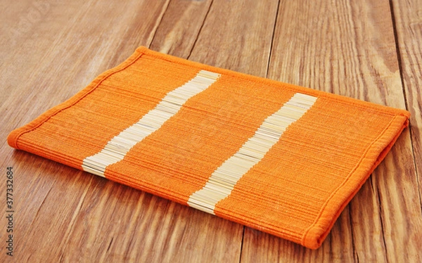 Fototapeta Orange bamboo placemat folded on wooden table.