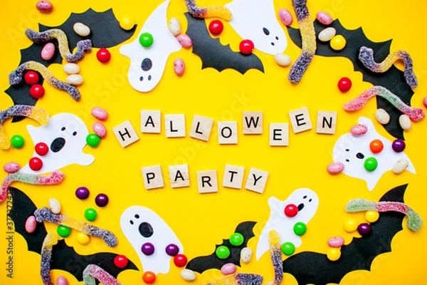 Fototapeta inscription from wooden blocks Halloween party and frame made of paper homemade bats and paper ghosts and multicolored candies and worms from gummy