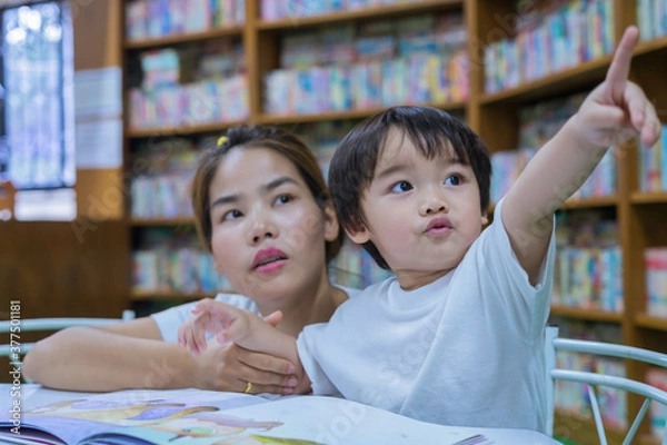 Fototapeta Asian young mother with little boy reading book together in library. Happy family. Parent educating children. Pre-school learning concept.