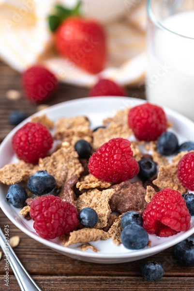 Fototapeta Granola with blueberries and raspberries in white bowl on dark white desk.