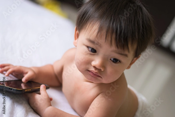 Fototapeta Little boy playing smartphone on the bed