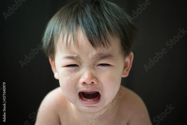 Fototapeta An Asian boy is crying on a black background