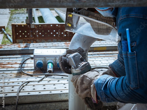 Fototapeta Worker is using electric wheel grinding on steel pipe structure in factory.