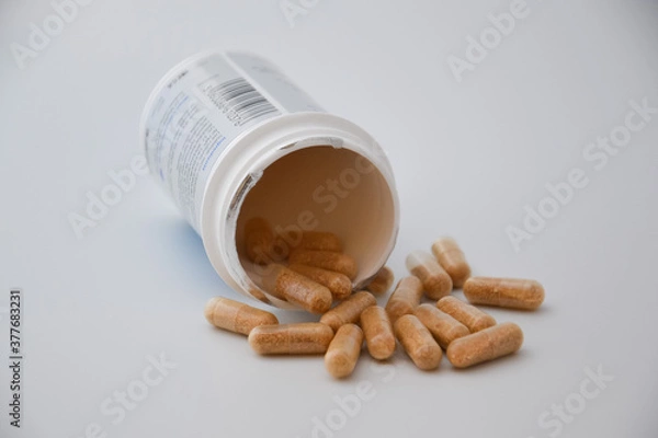 Fototapeta Close up medication bottle and natural pills spilled on white background. Medication and prescription pills flat lay background