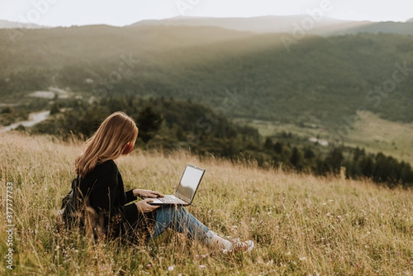 Fototapeta Woman with mask working on laptop on remote location in nature