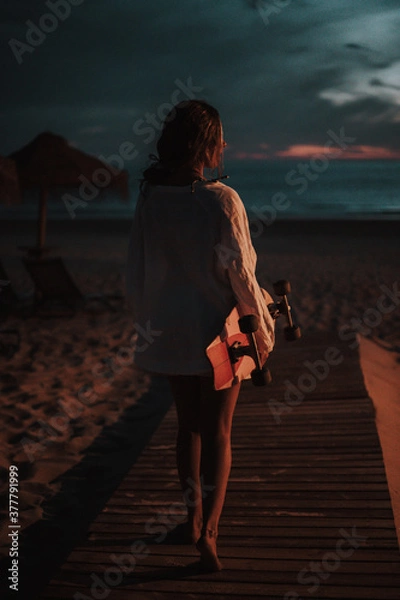 Obraz Chica veraniega morena en la playa naturaleza cañas de bambu con skateboard y bikini disfrutando de la hora dorada del atardecer