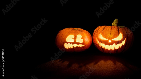Obraz Two Halloween pumpkins with glowing eyes and mouth on a black background with copy space. One pumpkin with a scary face, another with a scared face