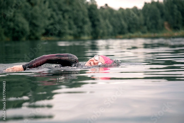Obraz A woman athlete in a pink cap floats on the lake. Sports swimming triathlon.