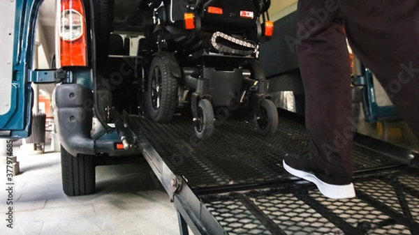 Fototapeta Wheelchair going into vehicle using ramp. Driver is helping to push it up.