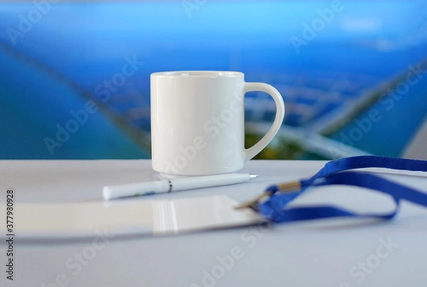 Fototapeta White cup, badge and pen on white table, soft blue background, business style