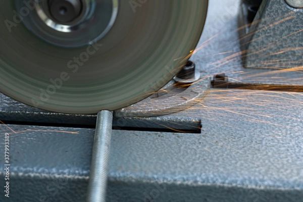 Fototapeta The angle grinder cuts the metal pin. The angle grinder is mounted on a stand. Sparks fly from under the disk.