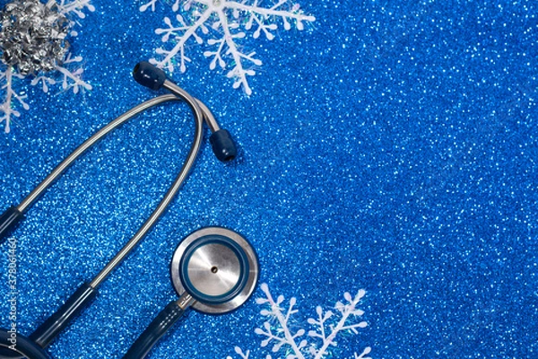 Fototapeta Blue Stethoscope and white snowflakes close-up on the left on a blue holiday background with glitter.The view from the top.