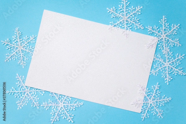 Fototapeta White sheet of paper on a blue background in the center, white snowflakes around the sheet. Empty space for entries.The view from the top