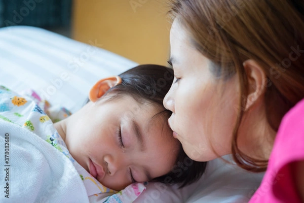Fototapeta Asian cute little boy patient is sleeping on the sickbed and the face with tears, his mother kissed him on the forehead in the patient room in hospital. Healthcare medical and people concept.