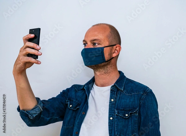 Fototapeta Man wearing a custom design face mask takes a selfie with his mobile phone.