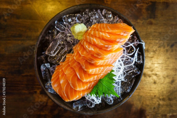 Fototapeta salmon shashimi - japanese raw food with wasabi on ice and sliced radish in black bowl