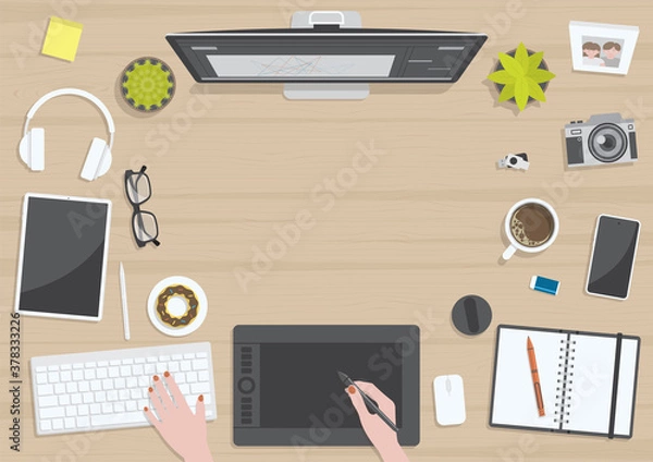 Fototapeta Wood textured table from top view with hands of woman drawing on digital graphic tablet with monitor, camera, tablet, headphones and gadgets, design for work from home concept