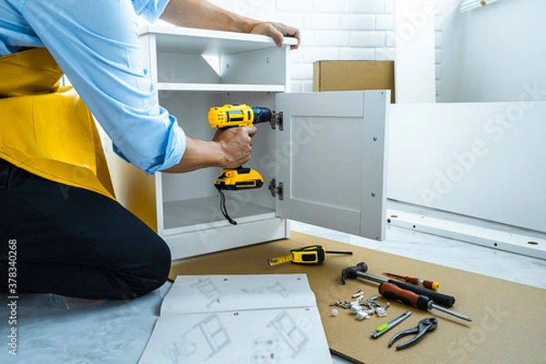 Fototapeta Man doing renovation work at home drilling wood with drill tack on locker