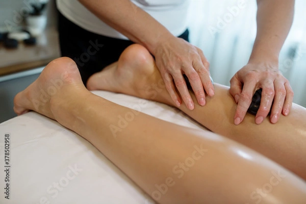 Obraz Masażysta w gabinecie kosmetycznym wykonuje masaż kamieniami młodej kobiecie w celu rozluźnienia ciała i drenowania limfy
