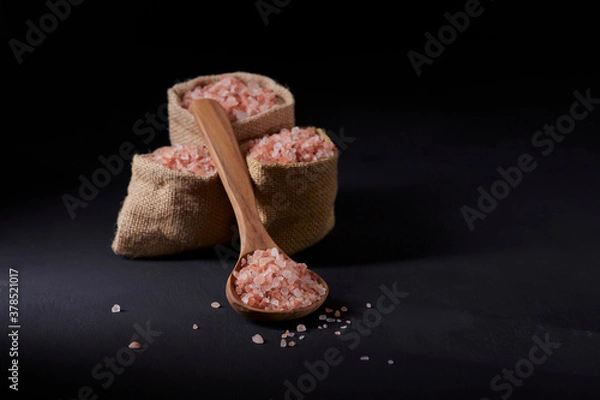 Fototapeta Himalayan salt, thick and pink, in three jute bags along with a wooden spoon with salt. All on a black background.
