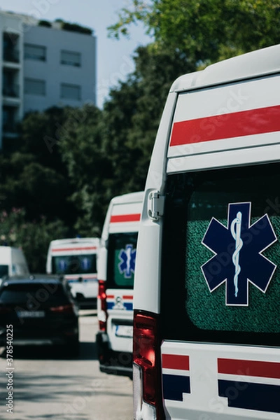 Fototapeta Vertical shot of the rear side of a white ambulance van, parked in Split, Croatia amid the coronavirus outbreak. Multiple vans lined up, healthcare symbols on their doors