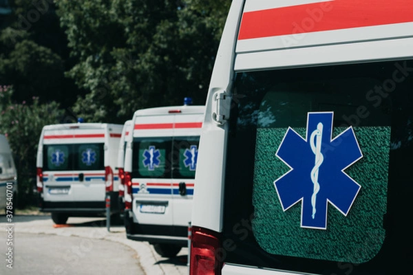 Fototapeta Multiple white ambulance vans parked together in Split, Croatia amid the coronavirus pandemic. Global healthcare symbol on their door windows