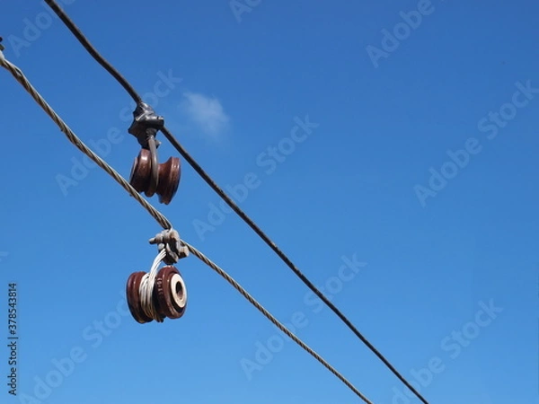 Fototapeta Brown insulators are damaged. An old electric fuse is hanging on a potentially dangerous low voltage line. On the blue sky background with white clouds. Selective focus