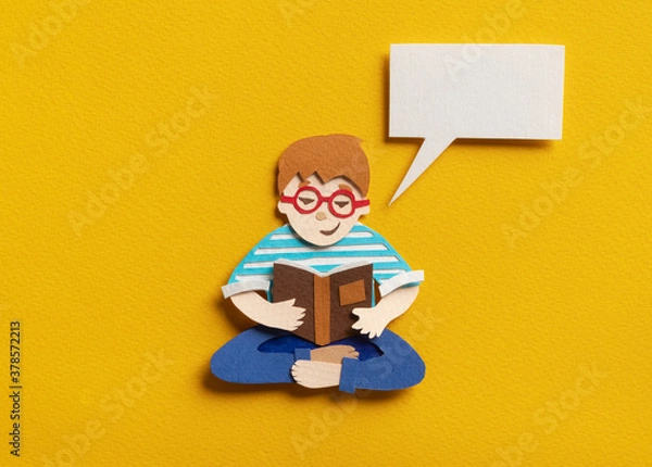 Fototapeta Smart boy in glasses sitting in lotus pose and learning new educational material. Smiling guy with empty speech bubble. Hand cut paper illustration on yellow background