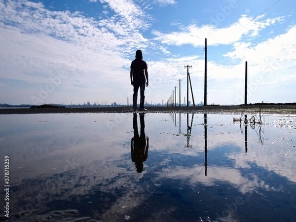 Obraz 電柱のある海で遠くを眺めている人と水面に映るリフレクション