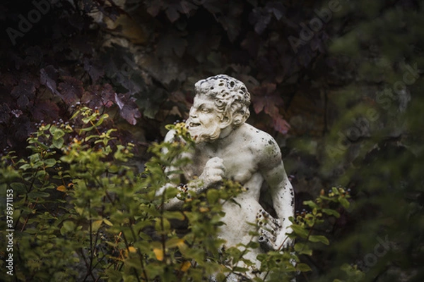 Obraz White statue sculpture of Pan the Greek god with a flute in his hand hiding behind foliage looking cheeky