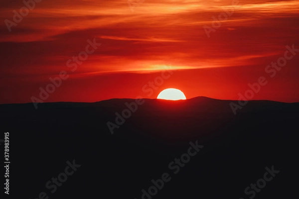 Fototapeta Beautiful image of the sun setting behind the mountains on a hot summer day
