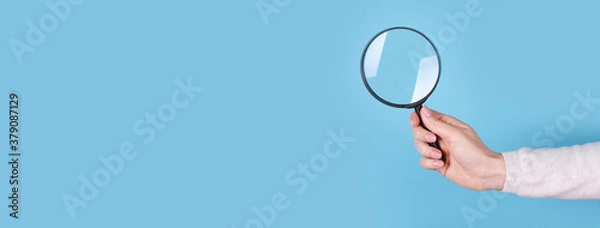 Obraz Magnifying glass in hand on a blue background, copy space template, banner.
