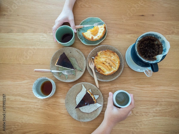Fototapeta Variety of sweet bakery dishes on wood table ,two hands hold cup of beverage from opposite side.Top view,Concept for food bakery and cafe.