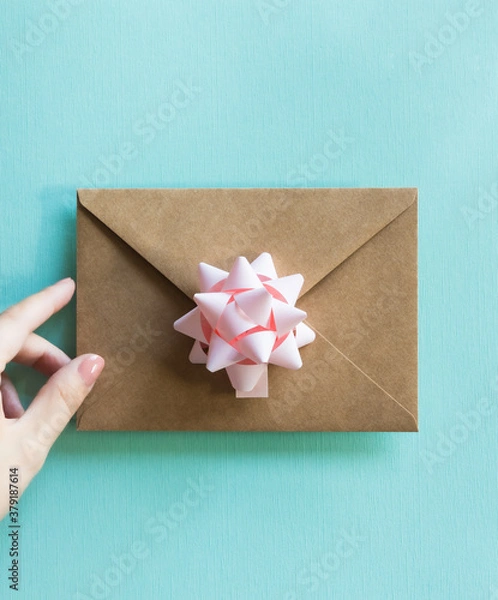 Fototapeta Kraft envelope with pastel pink bow in woman's hand on turquoise background. 