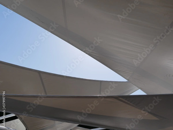 Fototapeta Large white polymer cloths of triangular shape are stretched over the beach against the blue sky. Creating shade on the beach on a Sunny summer day.