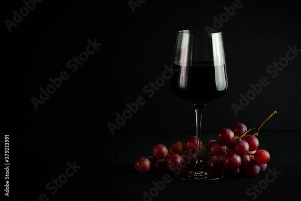 Obraz glass with red wine on a dark background and a bunch of red grapes.