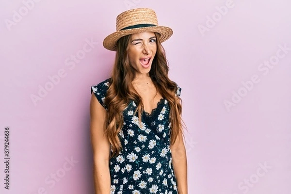 Fototapeta Młoda brunetka kobieta w letnim kapeluszu mrugając, patrząc w kamerę z sexy wyrazem twarzy, wesołą i szczęśliwą twarzą.