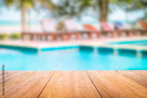 Fototapeta Image of wood table in front of a swimming pool blurred background. Brown wooden desk empty counter in front of the poolside on beautiful beach resort and outdoor spa.
