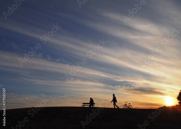 Obraz 夕焼けを見るためにベンチに座っている人と自転車で駆けつけた人のシルエット