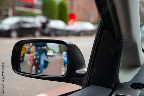 Fototapeta Blurred defocused photo. People on the bicycles in the city traffic. View in the side mirror of the car.