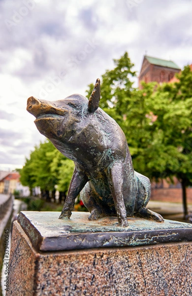 Fototapeta Sitting pig as a bronze statue on the canal bridge in the city of Wismar.