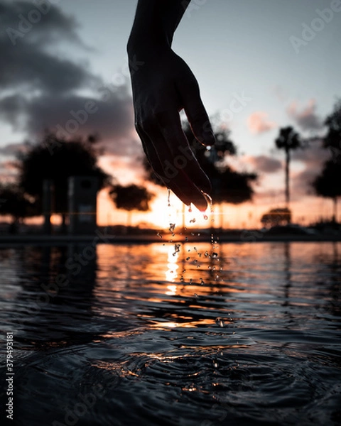 Fototapeta sunset on the river with hand dripping water