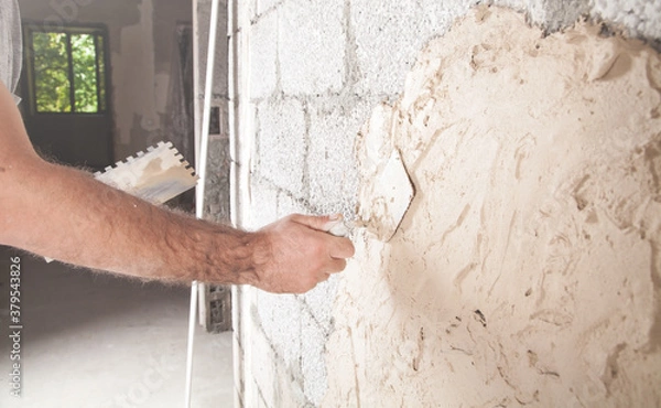Fototapeta Man is applying putty on a wall. Renovating house