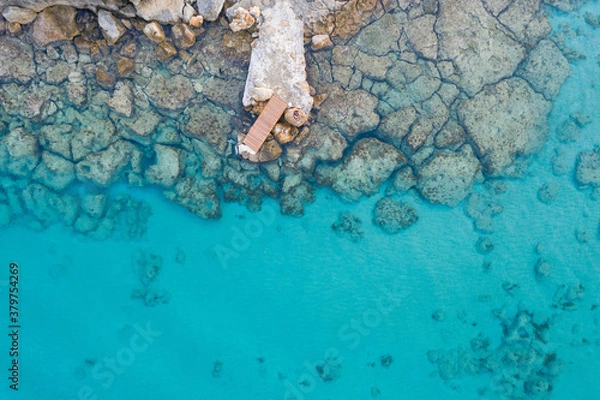 Obraz An aerial view of the beautiful Mediterranean Sea, with a wooden pier and a rocky shore, where you can see the textured underwater corals and the clean turquoise water of Protaras, Cyprus	