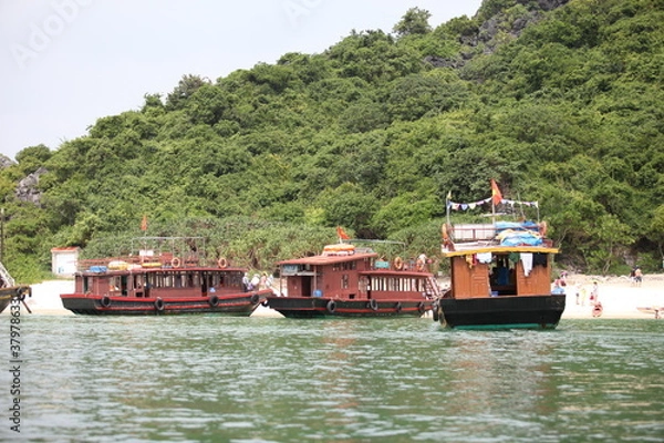 Fototapeta Cat Ba, Vietnam - November 19, 2019 : unk boat cruising in Lan Ha Bay near Ha Long Bay with karst limestone mountains in background.