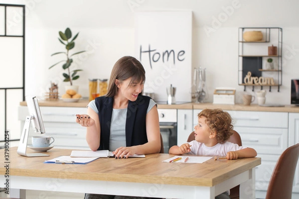 Fototapeta Working mother with little son in kitchen at home
