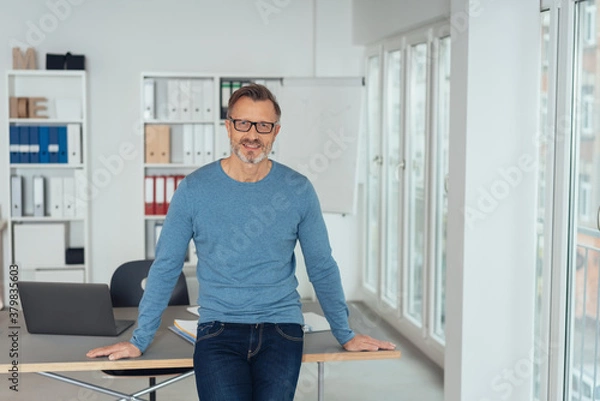 Fototapeta Relaxed businessman perched on an office table